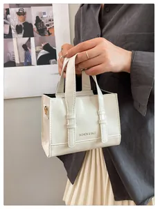 Detail view of a white leather handbag with sleek handles and fashion logo print
