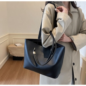 Close-up of a large black tote bag with fine matte texture and pale gold metal details