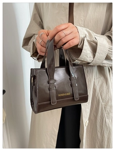 Detail of a dark brown glossy leather handbag with gold Fashion and Bags lettering