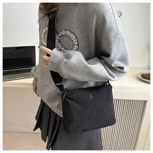 Détail du sac bandoulière en nylon noir avec logo métallique argenté et sangle réglable