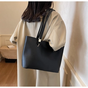 Close-up of a minimalist black tote bag with gold metal hardware details on the strap