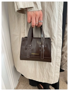 Detailed close-up of dark brown oil wax leather handbag with fashion gold lettering