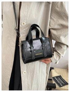 Fashionable black faux leather crossbody bag styled on a beige trench coat