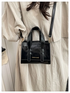 Detail of black wax leather handbag with gold lettering on a trench coat model