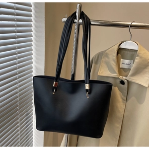 Close-up of minimalist black leather tote bag featuring gold ring strap connectors