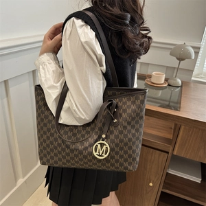 Classic dark brown tote bag with M-pattern print and gold pendant on female model