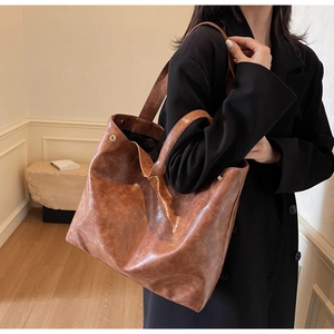 Brown vintage faux leather tote bag with wide shoulder strap and metal rivets on model