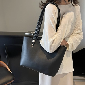 Minimalist black tote bag in soft leather with thin straps and elegant gold hardware