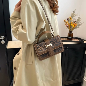 Détail du sac à main léopard vintage avec boucle dorée porté sur un trench-coat clair