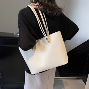 Minimalist beige PU leather tote bag with gold hardware shown on shoulder of a model