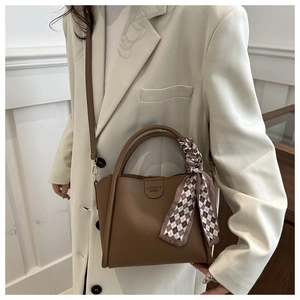 Détail du sac seau en cuir marron foncé avec foulard en soie et longue bandoulière