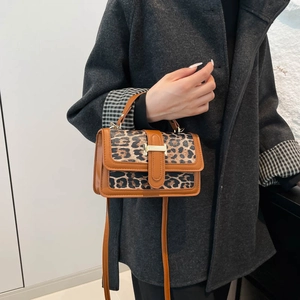 Détail d'un sac léopard avec fermoir en H doré et poignée en cuir sur un manteau gris