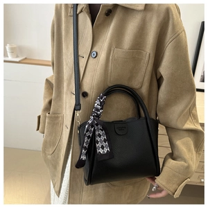 Détail du sac seau en cuir grainé noir avec un foulard décoratif à losanges sur l'anse