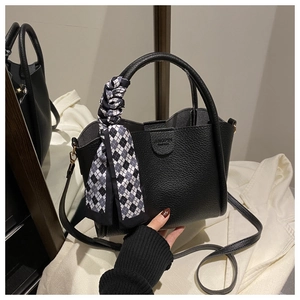 Détail d'un sac seau en cuir noir grainé avec poignées et foulard en soie à carreaux