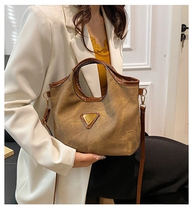 Detail view of a vintage brown crossbody bag with a triangular metal plaque and fine stitching