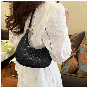 Détail du sac demi-lune noir à motif croco porté avec une robe en dentelle