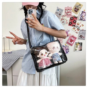 Detail view of a black ita bag with clear PVC window showing two plush dolls inside