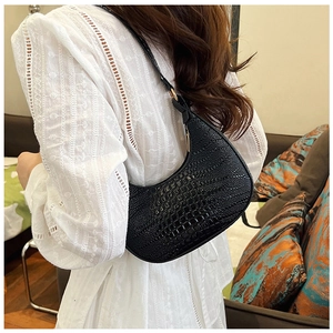 Détail d'un sac d'épaule noir avec gaufrage crocodile porté avec une chemise en dentelle