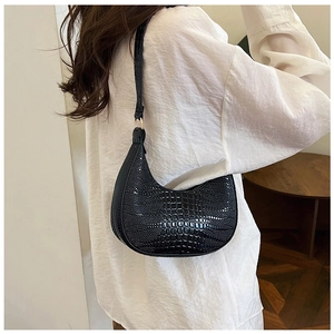 Modèle portant un sac hobo noir à motif crocodile et détails dorés pour un look chic