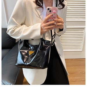 Glossy black handbag with golden triangle decor shown on model in white blazer