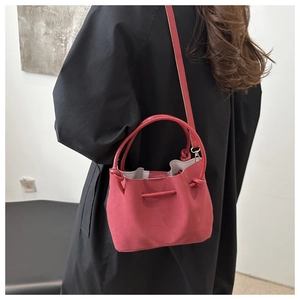 Detail of elegant red suede bucket bag with drawstring closure and slim strap on black coat