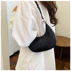 Détail du sac demi-lune en cuir crocodile noir porté à l'épaule pour un look rétro