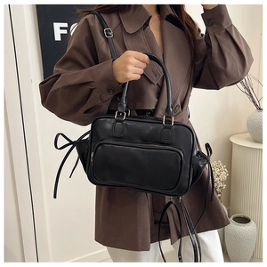Close-up of black matte leather handbag featuring side bow details and gold hardware