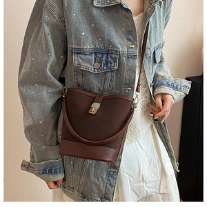 Detailed view of brown bucket bag with golden twist lock and reinforced base worn by model