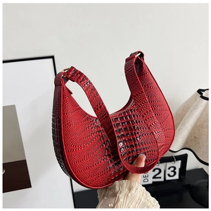 Détail d'un sac demi-lune rouge en cuir gaufré crocodile avec anneaux dorés élégants
