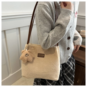 Detail of plush beige bucket bag with brown leather straps and cute bear charm pendant
