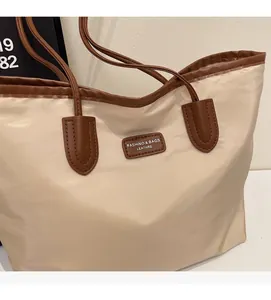 Detail of a large capacity tote bag with beige nylon body and brown leather handles