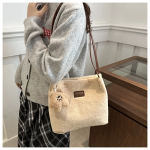 Detail of plush cream bucket bag with brown strap and cute bear charm in cozy home setting