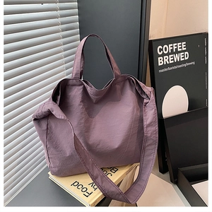 Dettaglio di una borsa tote viola in tela testurizzata su libri con luce soffusa dalla finestra