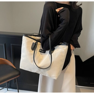 Detail view of large tote bag with black contrast handles and brand leather patch