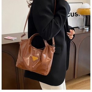 Detail view of brown glossy shoulder bag with vintage oil-wax leather texture and metal logo