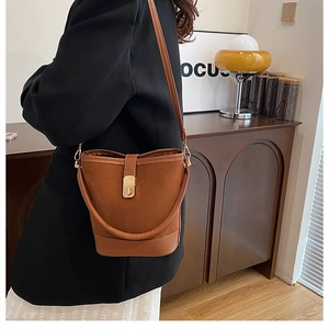 Detail of brown suede and leather bucket bag with gold metal buckle and long shoulder strap