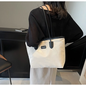 Close-up of cream nylon tote bag showing black logo patch and slim shoulder straps