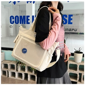 Dettaglio della borsa tote in tela con tasca a rete, badge blu e tracolla regolabile