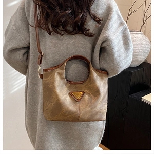 Detail shot of vintage brown leather handbag with metal logo on a model's shoulder