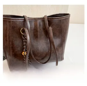 Detail of dark brown tote bag showing natural faux leather texture and golden charm