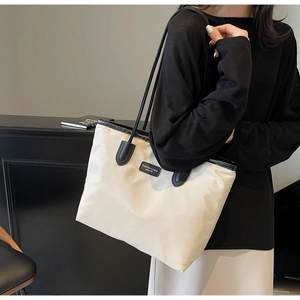 Detail view of the durable nylon tote bag featuring a leather logo patch and sturdy handles