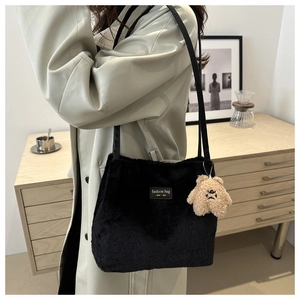Close-up of fluffy black plush shoulder bag with a cute brown teddy bear charm and logo tag