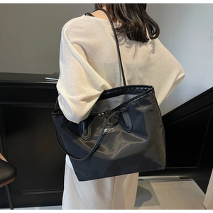 Detail of black nylon tote bag with leather straps and logo label in a street setting