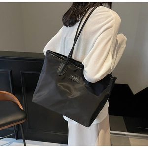 Close-up of a large black nylon tote bag with leather logo tag shown on model