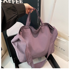 Dettaglio di una grande borsa tote viola in nylon con manici corti e tracolla larga