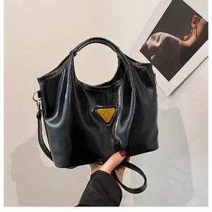 Detail view of black patent leather tote bag with gold triangle logo and top handles