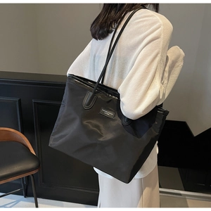 Detail view of black nylon tote bag on shoulder showing sleek texture and minimalist logo tag