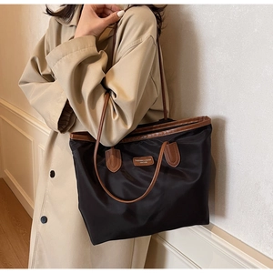 Detail of black nylon tote bag featuring brown faux leather trim and fashion label