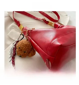 Detail of red pebbled leather shoulder bag with teddy bear charm and woven rope accent