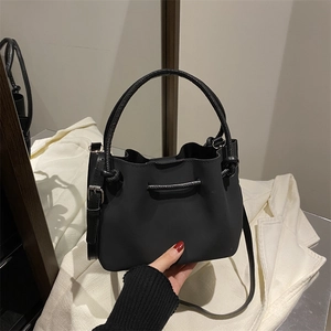 Minimalist black matte bucket bag with circular handle and adjustable shoulder strap